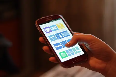 Hand holding a Samsung phone showing a grid of app icons
